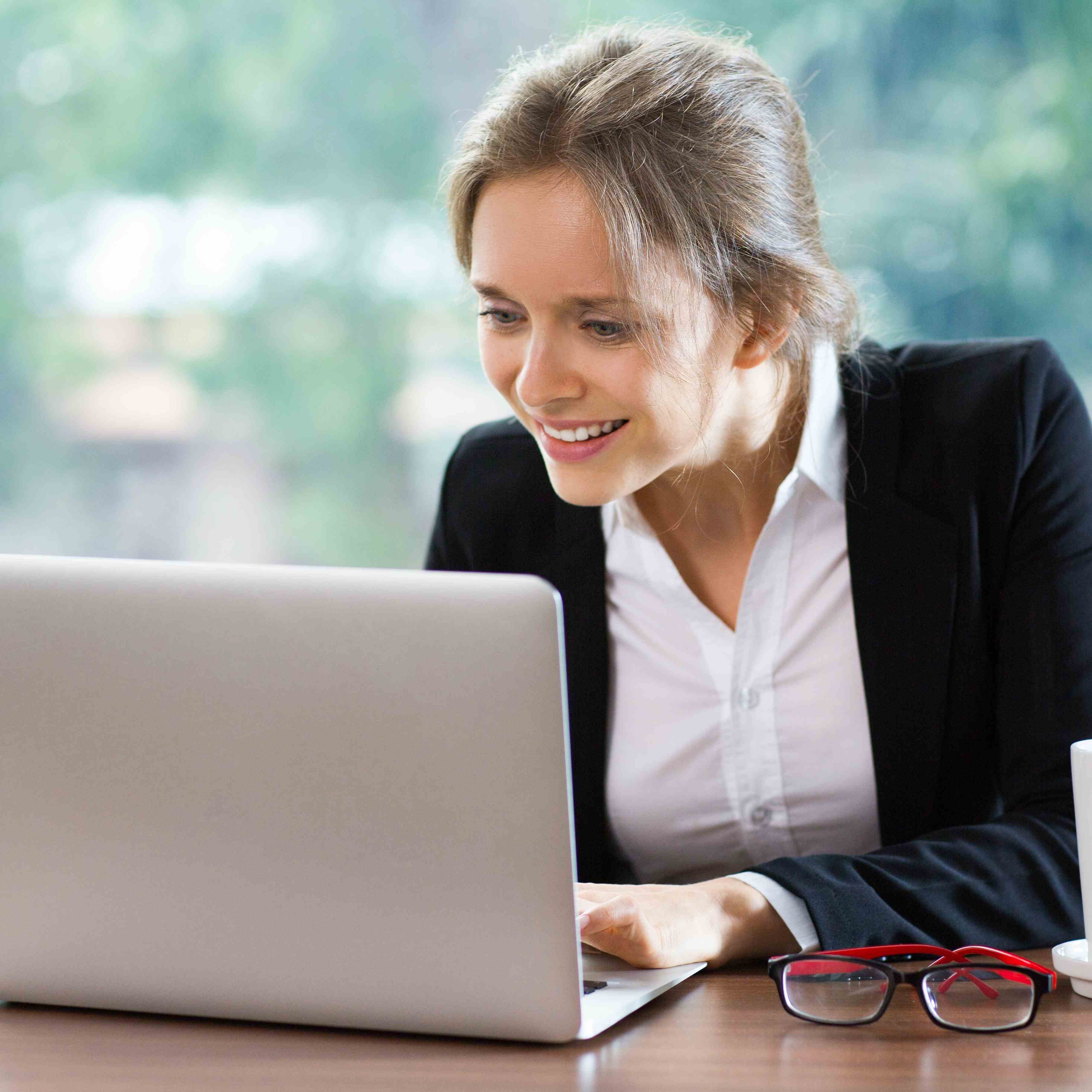 Woman smiling while writing MBA essay on laptop